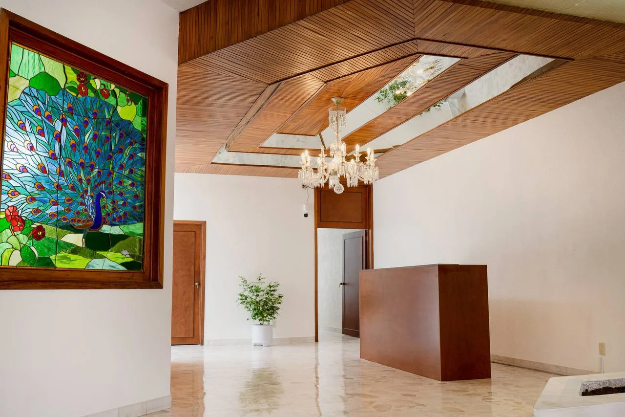 Recepción de Violeta con vitral de pavo real, plafón de madera y un candil de cristal