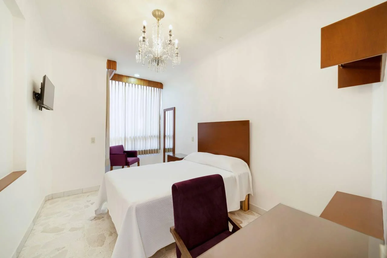 Habitación sencilla, cama matrimonial y asiento violeta